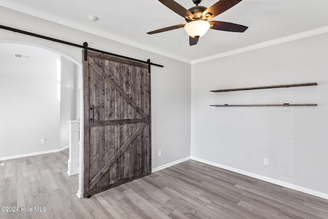 unfurnished room with a barn door, hardwood / wood-style flooring, ceiling fan, and crown molding