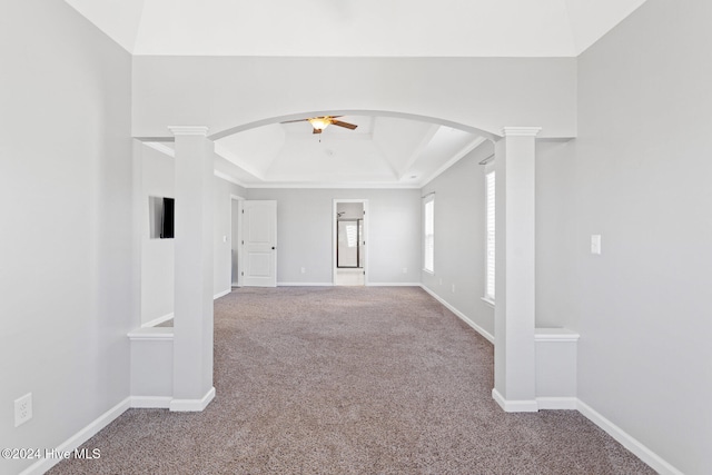 carpeted empty room with a raised ceiling, ceiling fan, and ornate columns