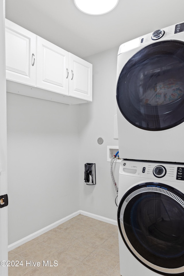 clothes washing area with cabinets, light tile patterned floors, and stacked washer / drying machine