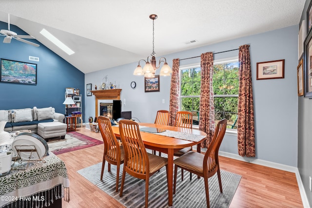 dining space with vaulted ceiling with skylight, ceiling fan with notable chandelier, a textured ceiling, and light hardwood / wood-style flooring