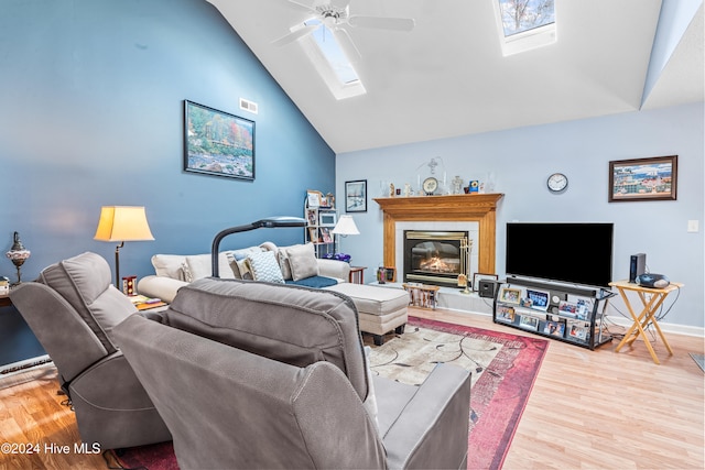 living room featuring hardwood / wood-style floors, ceiling fan, high vaulted ceiling, and a skylight