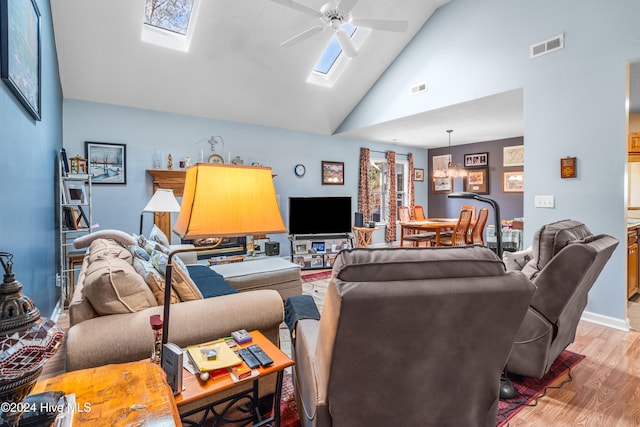 living room featuring high vaulted ceiling, light wood-type flooring, a skylight, and ceiling fan