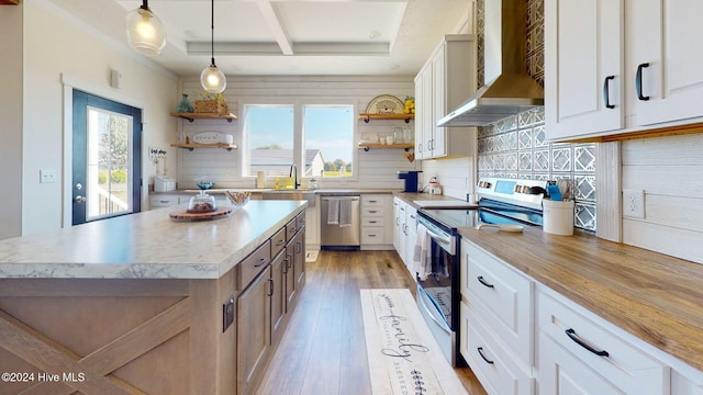 kitchen with stainless steel appliances, wall chimney exhaust hood, hanging light fixtures, a kitchen island, and white cabinetry