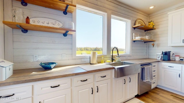 kitchen with wood walls, white cabinetry, sink, and stainless steel dishwasher