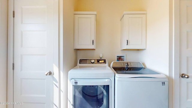 clothes washing area with washing machine and clothes dryer and cabinets