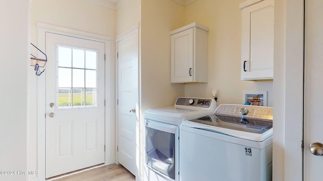 clothes washing area featuring cabinets, light wood-type flooring, and washer and clothes dryer