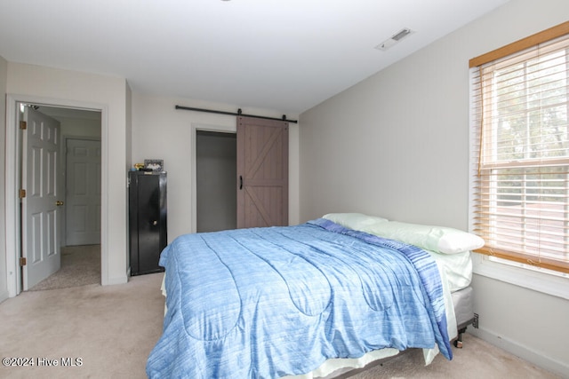 bedroom with multiple windows, light carpet, and a barn door