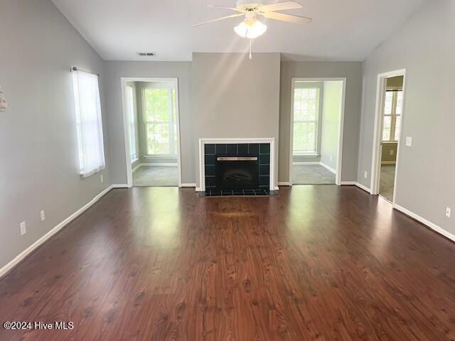 unfurnished living room with dark wood-type flooring, a wealth of natural light, ceiling fan, and a fireplace