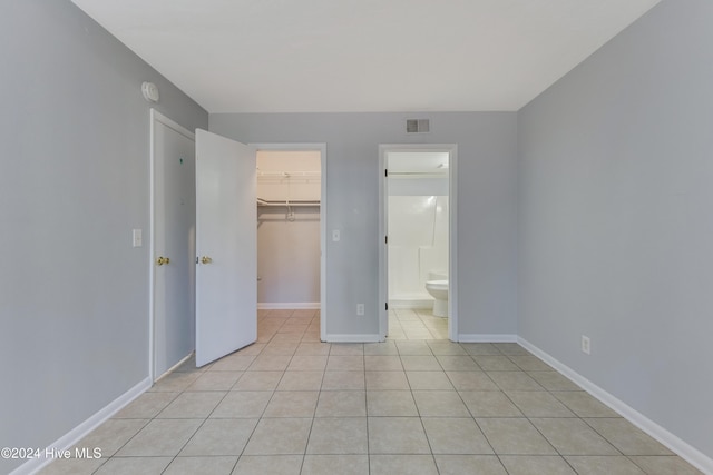 unfurnished bedroom with ensuite bath, light tile patterned floors, a closet, and a spacious closet