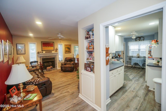 living room featuring a tile fireplace, ceiling fan, sink, and light hardwood / wood-style floors