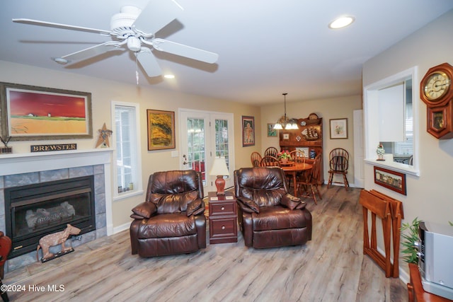 living room featuring french doors, ceiling fan with notable chandelier, light hardwood / wood-style floors, and a tile fireplace