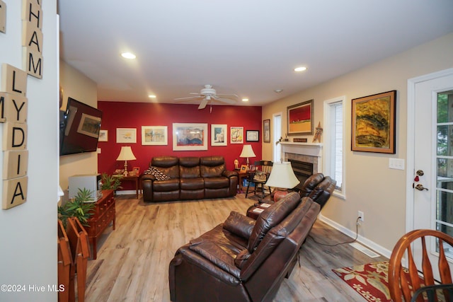 living room featuring a tiled fireplace, light hardwood / wood-style flooring, and ceiling fan