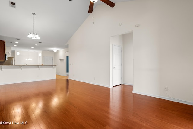 unfurnished living room with wood-type flooring, ceiling fan with notable chandelier, and high vaulted ceiling