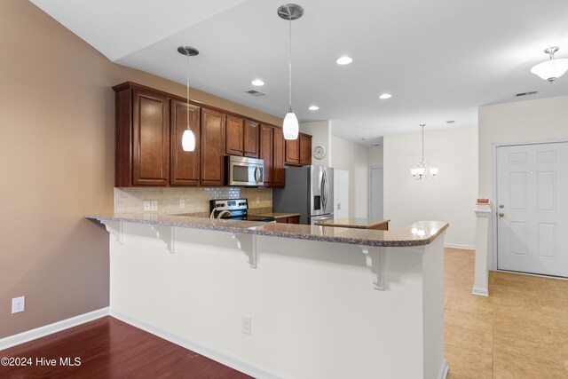 kitchen with kitchen peninsula, stainless steel appliances, hanging light fixtures, and a breakfast bar area