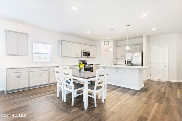 kitchen with stainless steel appliances, dark hardwood / wood-style flooring, pendant lighting, a kitchen bar, and a center island with sink