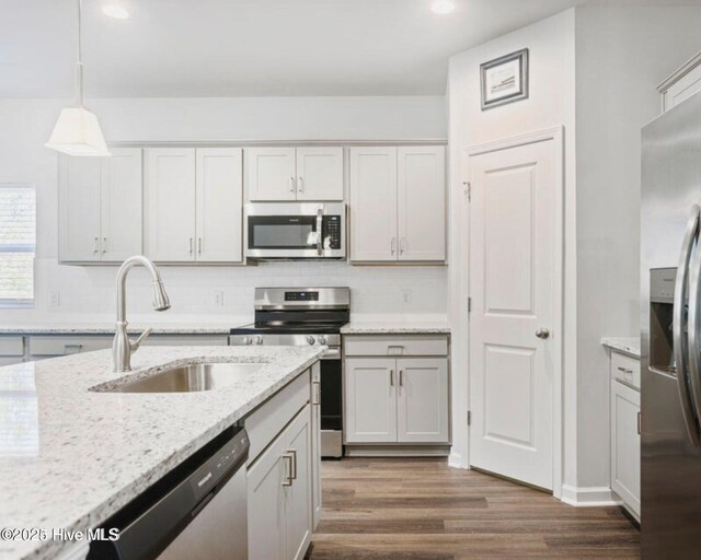 kitchen with appliances with stainless steel finishes, light stone counters, sink, dark hardwood / wood-style floors, and hanging light fixtures