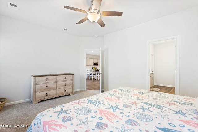 bedroom with ceiling fan, light colored carpet, and ensuite bathroom