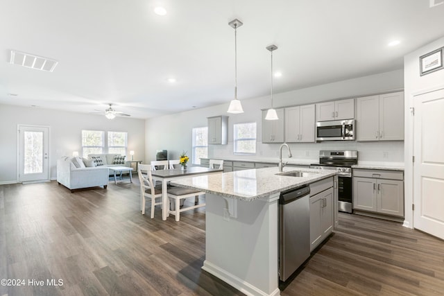 kitchen with stainless steel appliances, sink, decorative light fixtures, gray cabinets, and an island with sink