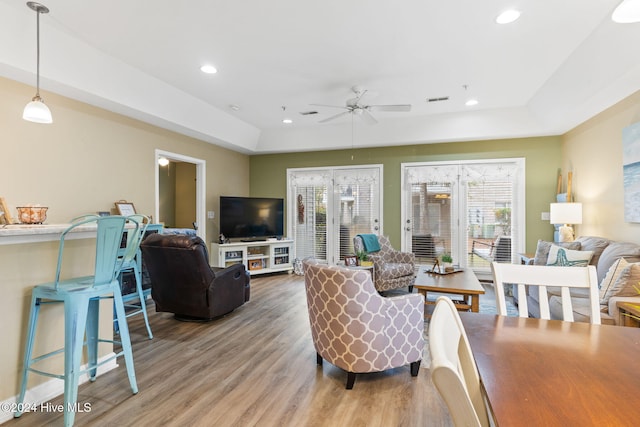 living room with hardwood / wood-style floors, a raised ceiling, and ceiling fan