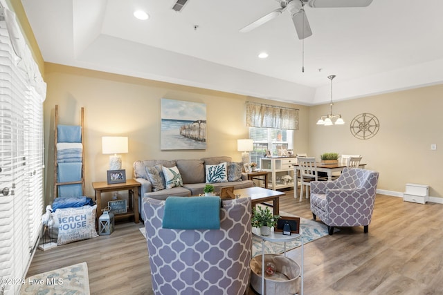 living room with ceiling fan with notable chandelier, wood-type flooring, and a tray ceiling