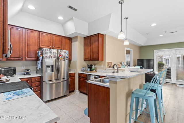 kitchen featuring a breakfast bar, appliances with stainless steel finishes, decorative light fixtures, light hardwood / wood-style floors, and kitchen peninsula