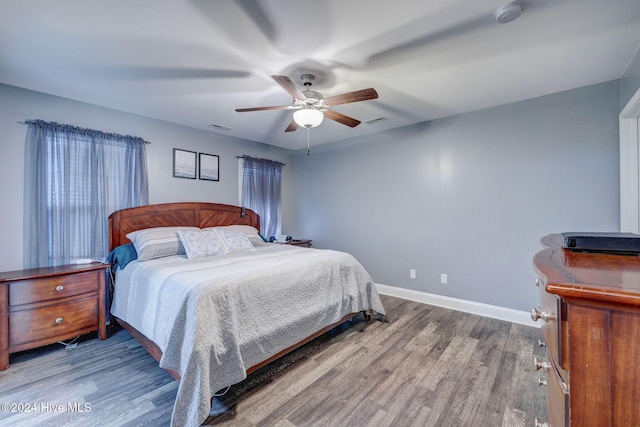 bedroom with a ceiling fan, visible vents, wood finished floors, and baseboards