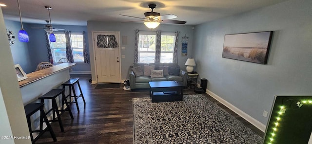 living area featuring dark wood-type flooring, a ceiling fan, and baseboards