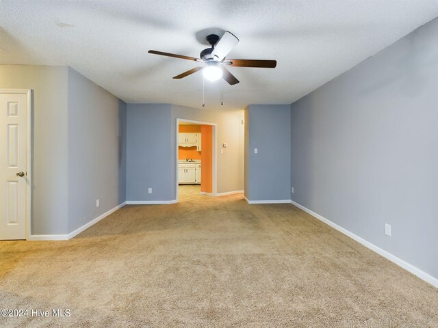 interior space with a textured ceiling, light colored carpet, ensuite bath, and ceiling fan