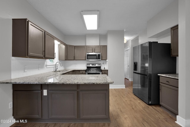 kitchen featuring sink, light stone counters, kitchen peninsula, appliances with stainless steel finishes, and light wood-type flooring