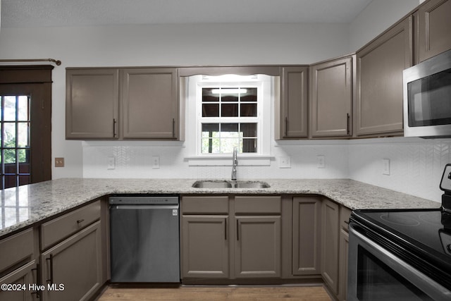 kitchen with stainless steel appliances, light stone countertops, sink, and light wood-type flooring