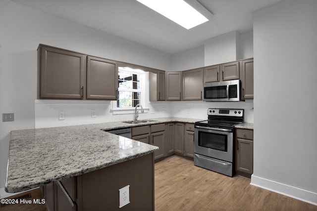 kitchen featuring stainless steel appliances, light hardwood / wood-style floors, light stone counters, kitchen peninsula, and sink