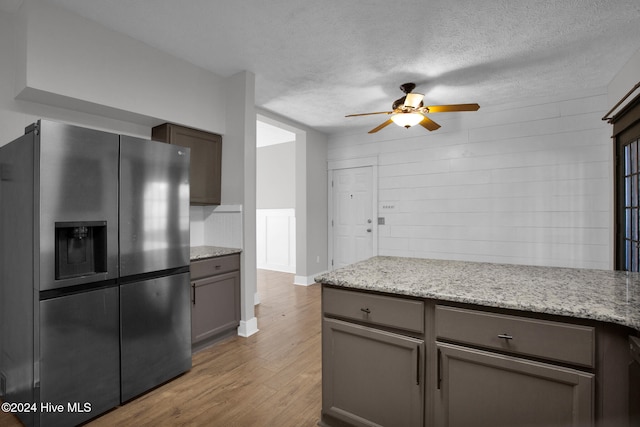 kitchen with a textured ceiling, stainless steel fridge with ice dispenser, light stone countertops, ceiling fan, and light hardwood / wood-style flooring