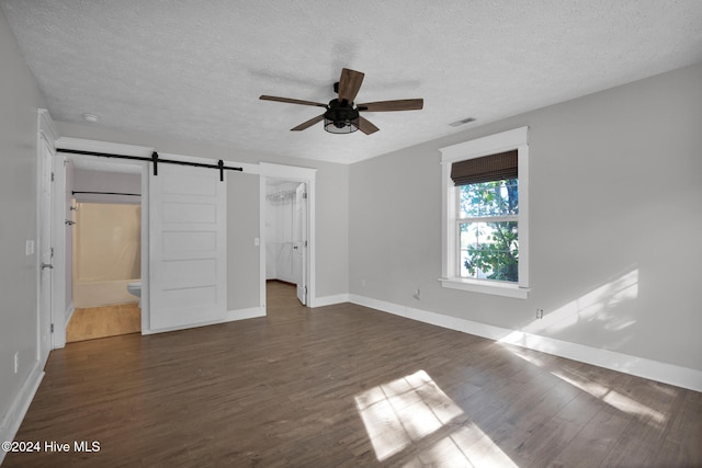 unfurnished bedroom featuring a barn door, ensuite bath, a closet, and dark wood-type flooring