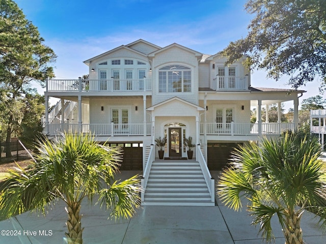 coastal home featuring a balcony, an attached garage, covered porch, stairs, and french doors