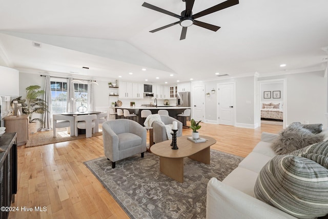 living room featuring sink, vaulted ceiling, ceiling fan, ornamental molding, and light wood-type flooring