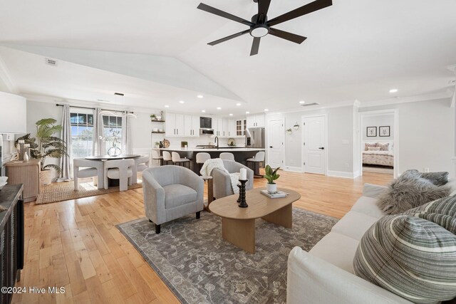 living room with ceiling fan, light wood-type flooring, and vaulted ceiling