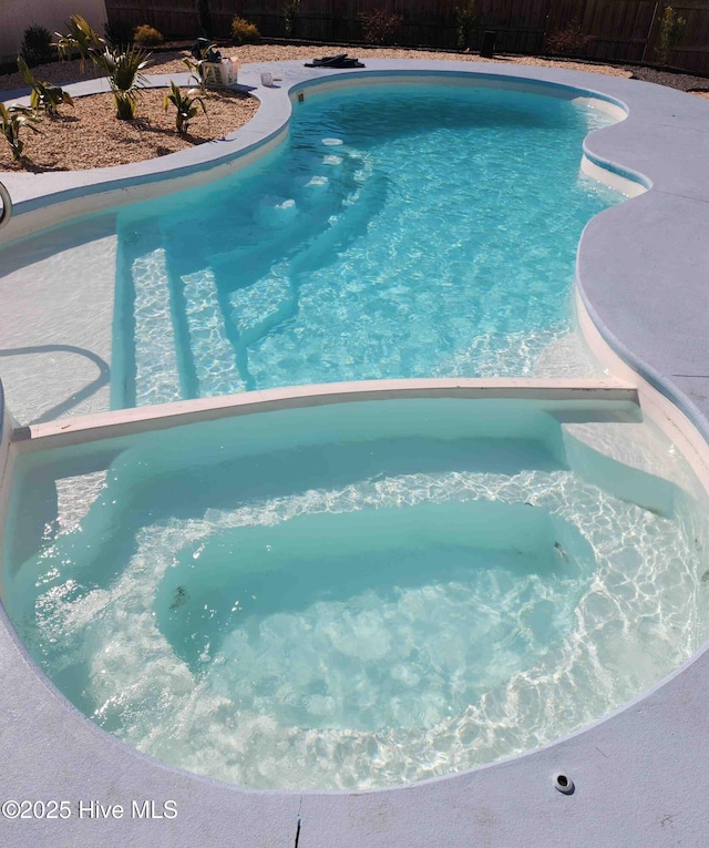 view of swimming pool with fence, a fenced in pool, and an in ground hot tub