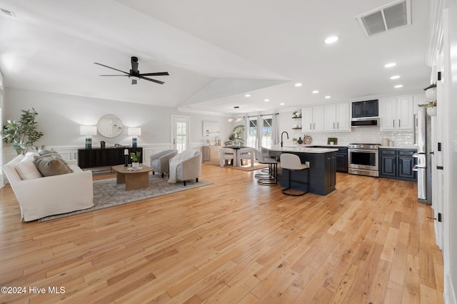 living room with ceiling fan, light hardwood / wood-style flooring, vaulted ceiling, and sink