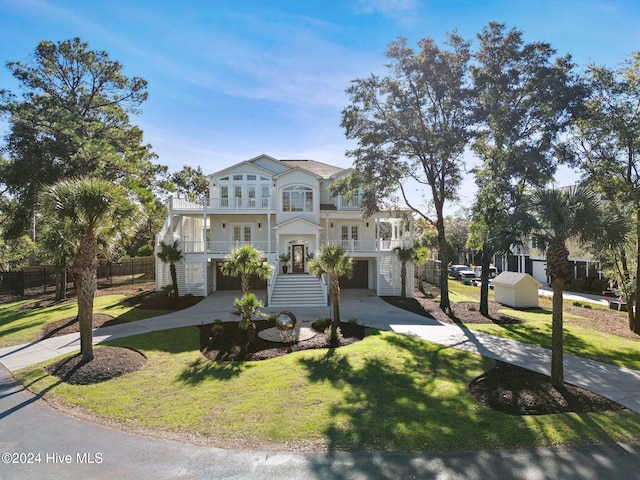 coastal home with driveway, a balcony, fence, french doors, and a front lawn