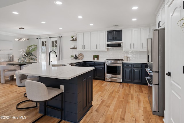 kitchen with white cabinets, a peninsula, stainless steel appliances, a kitchen bar, and a sink