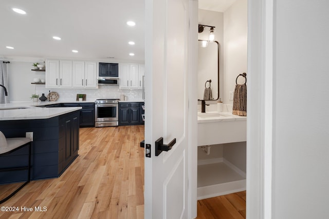 kitchen with backsplash, sink, stainless steel stove, light hardwood / wood-style floors, and white cabinetry