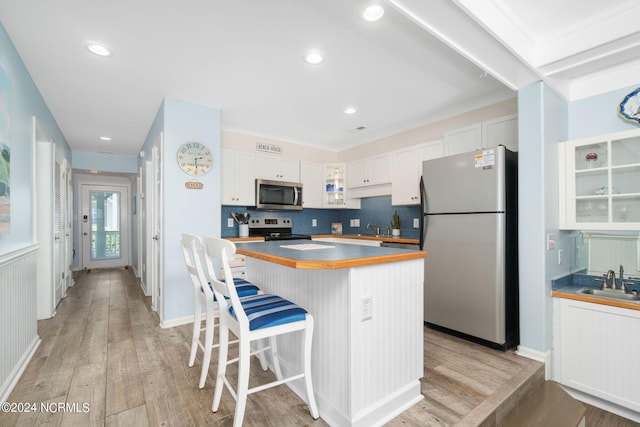 kitchen with white cabinetry, light wood-type flooring, appliances with stainless steel finishes, a kitchen breakfast bar, and a kitchen island