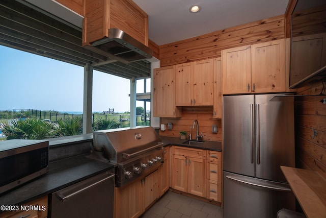 kitchen featuring light brown cabinetry, sink, stainless steel appliances, and wood walls