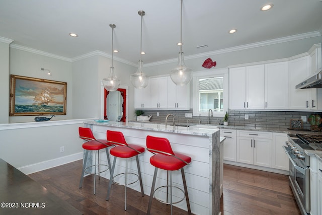 kitchen featuring white cabinetry, stainless steel stove, pendant lighting, light stone countertops, and a kitchen island with sink