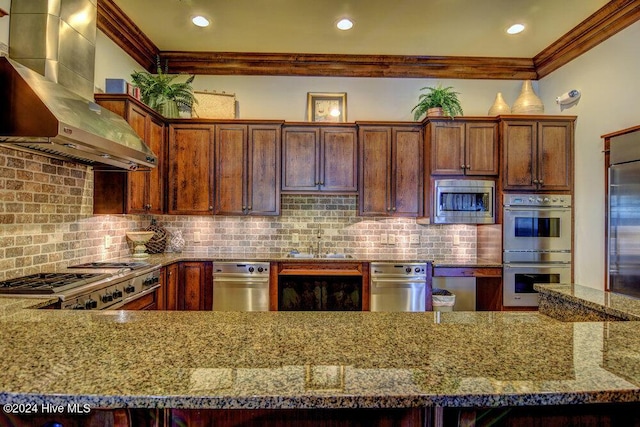 kitchen with crown molding, tasteful backsplash, stone countertops, built in appliances, and wall chimney exhaust hood