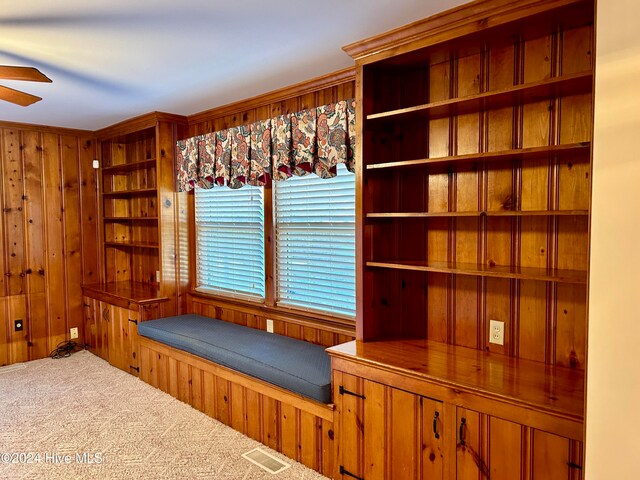 interior space featuring carpet flooring, wood walls, ceiling fan, and crown molding