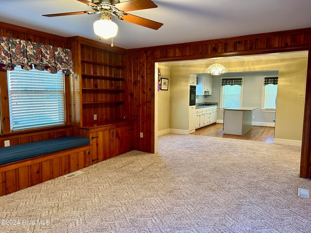 unfurnished living room featuring wood walls, a healthy amount of sunlight, and light carpet