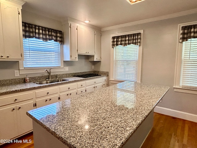 kitchen featuring sink, ornamental molding, light stone countertops, a kitchen island, and dark wood-type flooring