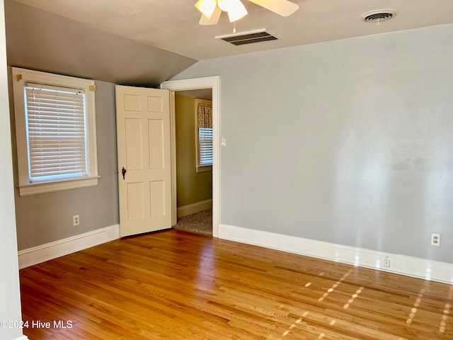 empty room featuring a healthy amount of sunlight, vaulted ceiling, hardwood / wood-style flooring, and ceiling fan