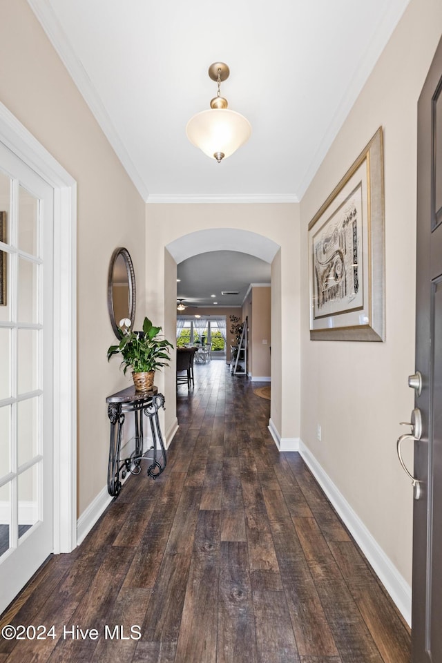 hall featuring ornamental molding, arched walkways, wood-type flooring, and baseboards